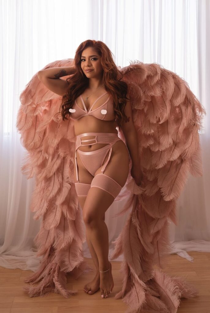 In this breathtaking artistic boudoir photograph captured by Limitless Boudoir in El Dorado Hills, California, a woman is featured wearing magnificent 6-feet tall pink feathered angel wings. This photo embodies the perfect setting for women in the Sacramento area looking for artistic, romantic, and luxurious boudoir photography. The woman's delicate pink lingerie, combined with the magnificent wings and angelic setting, create an elegant and dreamy atmosphere. The soft lighting in the background provides a warm and relaxing ambiance, while the woman's emotional expression conveys feelings of calm and tranquility. The photograph exudes a sense of femininity, sophistication, and beauty, simultaneously capturing the freedom and power of a confident woman. This artistic and romantic boudoir photograph provides a beautiful memory to celebrate a woman's strength, sensuality, and elegance in a truly luxurious and breathtaking setting.